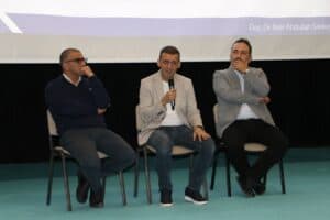 Basın merkezinde üç kişi panelde konuşma yapıyor, arka planda projeksiyon ekranı var.